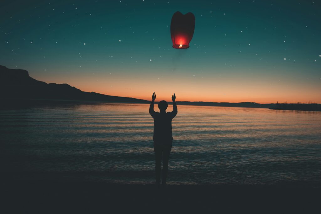 A person releases a glowing paper lantern into the sky, symbolizing letting go of burdens for peace and freedom.